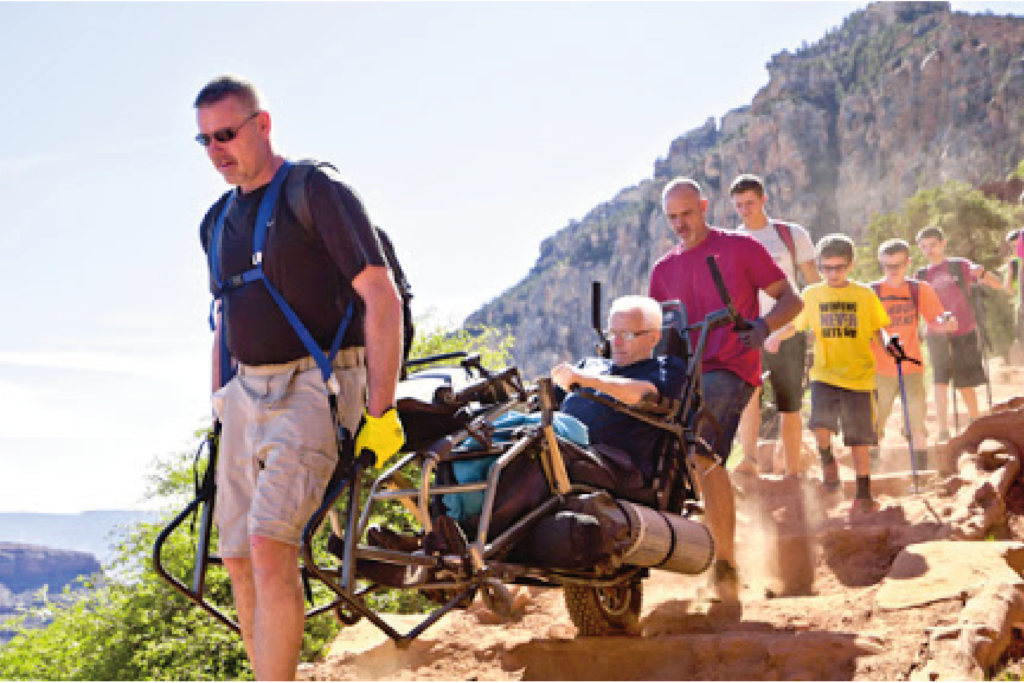 Group of hikers walking with a TrailRider on a cliff side.