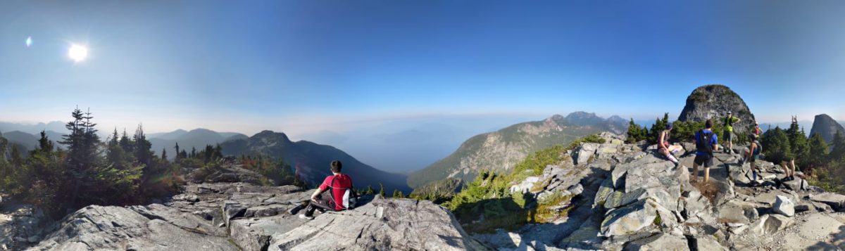 A young man sits on a mountain looking at the view.